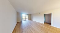 This single-story unit offers a thoughtfully organized layout across a comfortable footprint, comprising a living room, kitchen, bedroom, full bathroom, and two closets. The living room is a bright, open space anchored by light-toned hardwood flooring and a large sliding glass door that floods the room with natural light and provides direct views of mature trees and greenery outside. A small chandelier in the adjoining area adds a refined touch to the space.

The kitchen features white shaker-style cabinetry extending to the ceiling, granite-look countertops, a stainless steel sink, and a full suite of stainless steel appliances including an electric range and over-the-range microwave. The hardwood flooring continues seamlessly from the living area into the kitchen.

The bedroom is carpeted and receives natural light through a window with an outdoor view, offering a quiet and comfortable atmosphere. Two closets provide practical storage throughout the unit.

The bathroom is finished with white shaker cabinetry, granite-look countertops, a framed mirror, and a full tub-shower combination. Hardwood flooring extends into the bathroom, maintaining a consistent aesthetic throughout the unit. Overall, the space presents a clean, modern, and cohesive design.