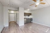 Located in Worcester, MA, this well-appointed single-floor unit makes efficient use of its compact footprint. The layout centers around an open-concept living, dining, and kitchen area unified by light gray laminate hardwood flooring that runs throughout. The kitchen is outfitted with dark gray cabinetry, a stainless steel refrigerator, a range, and a sink, all neatly arranged along one wall. A ceiling fan overhead serves the combined living and dining space, promoting airflow and comfort. Drop-panel ceilings are featured throughout the unit, adding a clean, uniform aesthetic. An entry hallway leads from the front door — where an electrical panel is conveniently accessible — into the main living area. Large windows with horizontal blinds allow natural light to fill the space and offer views of the surrounding Worcester streetscape. Baseboard heating units run along the perimeter walls, providing consistent warmth. The bathroom features warm-toned ceramic tile flooring, a toilet, and a bathtub with shower. A dedicated closet provides valuable storage. The unit's neutral gray and white color palette throughout creates a calm, cohesive atmosphere well-suited for comfortable urban living.