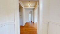 Located at 300 E 30th St in Baltimore, MD, this well-appointed single-floor residence offers four bedrooms, three bathrooms, a living room, and a dedicated kitchen across a generously sized layout. Rich hardwood flooring runs throughout the main living areas, hallways, and bedrooms, lending warmth and character to the space. The central hallways connect each room efficiently, with a decorative flush-mount light fixture adding a refined touch. The primary bedroom is notably spacious and includes a built-in closet, while additional bedrooms also feature closet storage and windows that invite natural light. The kitchen stands out with bold dark cabinetry accented by gold hardware, crisp white quartz-style countertops, a subway tile backsplash, stainless steel appliances including a gas range, dishwasher, and refrigerator, plus marble-look tile flooring and track lighting overhead. All three bathrooms continue the modern aesthetic with the same marble-look tile flooring, clean white walls, and contemporary fixtures. One bathroom features a tall window that frames an outdoor tree view, enhancing the sense of brightness. The living room offers an open, airy feel with hardwood floors and a globe pendant light. Throughout, the space balances classic architectural details with modern updates.
