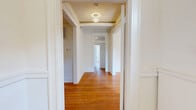Located at 300 E 30th St in Baltimore, MD, this well-appointed single-floor residence offers four bedrooms, three bathrooms, a living room, and a dedicated kitchen across a generously sized layout. Rich hardwood flooring runs throughout the main living areas, hallways, and bedrooms, lending warmth and character to the space. The central hallways connect each room efficiently, with a decorative flush-mount light fixture adding a refined touch. The primary bedroom is notably spacious and includes a built-in closet, while additional bedrooms also feature closet storage and windows that invite natural light. The kitchen stands out with bold dark cabinetry accented by gold hardware, crisp white quartz-style countertops, a subway tile backsplash, stainless steel appliances including a gas range, dishwasher, and refrigerator, plus marble-look tile flooring and track lighting overhead. All three bathrooms continue the modern aesthetic with the same marble-look tile flooring, clean white walls, and contemporary fixtures. One bathroom features a tall window that frames an outdoor tree view, enhancing the sense of brightness. The living room offers an open, airy feel with hardwood floors and a globe pendant light. Throughout, the space balances classic architectural details with modern updates.