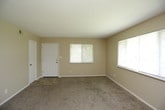 This single-floor residence offers a practical and comfortable layout designed for everyday living. The living area is generously sized, finished with warm beige carpet and neutral-toned walls that create a welcoming atmosphere. Large windows fitted with blinds allow natural light to fill the space while maintaining privacy. An adjoining room, also carpeted, features a ceiling fan with a light fixture and a closet with a bi-fold door, making it well-suited as a bedroom. A second carpeted bedroom provides additional flexibility, complete with its own closet and a window overlooking greenery outside.

The galley-style kitchen is thoughtfully equipped with an abundance of warm wood cabinetry offering generous storage above and below the counters. A double-basin sink, electric coil range with overhead ventilation, and a full-size refrigerator provide all essential appliances. Tile-style flooring runs throughout the kitchen, adding durability to the space.

The bathroom features tile-style flooring consistent with the kitchen, a soaking bathtub with tiled surround, and a clean, bright finish throughout. A hallway adjacent to the bathroom offers additional access and connectivity within the home. Overall, the space presents a functional and straightforward design with consistent finishes across all rooms.