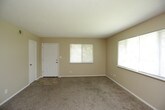 This single-floor residence offers a practical and comfortable layout designed for everyday living. The living area is generously sized, finished with warm beige carpet and neutral-toned walls that create a welcoming atmosphere. Large windows fitted with blinds allow natural light to fill the space while maintaining privacy. An adjoining room, also carpeted, features a ceiling fan with a light fixture and a closet with a bi-fold door, making it well-suited as a bedroom. A second carpeted bedroom provides additional flexibility, complete with its own closet and a window overlooking greenery outside.

The galley-style kitchen is thoughtfully equipped with an abundance of warm wood cabinetry offering generous storage above and below the counters. A double-basin sink, electric coil range with overhead ventilation, and a full-size refrigerator provide all essential appliances. Tile-style flooring runs throughout the kitchen, adding durability to the space.

The bathroom features tile-style flooring consistent with the kitchen, a soaking bathtub with tiled surround, and a clean, bright finish throughout. A hallway adjacent to the bathroom offers additional access and connectivity within the home. Overall, the space presents a functional and straightforward design with consistent finishes across all rooms.