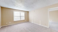 This single-floor residence offers a practical and comfortable layout with a warm, neutral color palette throughout. The kitchen is a functional highlight of the space, featuring rich dark wood cabinetry, granite-look countertops, and a full suite of stainless steel appliances including a refrigerator, range, microwave, and dishwasher. A peninsula counter provides additional workspace and serves as a natural divide between the kitchen and the adjoining living area. The flooring transitions from hardwood-style planks in the kitchen to plush wall-to-wall carpeting in the living and bedroom areas, lending a cozy feel underfoot. The living space is open and versatile, with warm beige walls and clean white baseboards that create a bright, welcoming atmosphere. The bedrooms are generously proportioned, each finished with soft carpet, textured ceilings, and windows fitted with blinds that allow for natural light while maintaining privacy. Ceiling fans are present, adding both comfort and air circulation. The bathroom is finished with clean white tile surrounding a full soaking tub and shower combination, complemented by built-in cabinetry offering ample storage. Throughout the unit, the design emphasizes functionality and ease of living in a cohesive, understated aesthetic.