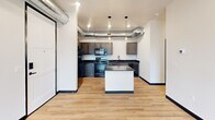 Located in the heart of Rapid City, SD, this modern 2-bedroom, 2-bathroom unit delivers a compelling blend of industrial and contemporary design across a well-organized single floor. Light hardwood flooring flows throughout, complemented by crisp white walls, bold black trim accents, and signature exposed silver ductwork that lends an urban, loft-inspired character to every room.

The kitchen is a functional centerpiece, featuring dark shaker-style cabinetry, black countertops, a full suite of black appliances including a range, dishwasher, and over-the-range microwave, and a central island for additional prep and dining space. Pendant lighting adds a refined touch overhead.

The spacious primary bedroom is a standout, boasting floor-to-ceiling windows on two walls that frame sweeping panoramic views of the Rapid City skyline and surrounding hills, allowing abundant natural light to fill the room. A ceiling fan adds comfort. The second bedroom also enjoys large sliding glass doors opening to a private balcony with city views.

Both bathrooms are finished with dark vanities, black countertops, and vessel sinks. One bathroom features a tub-shower combo. The unit also includes a hallway, closet, and utility room, rounding out a practical and stylish layout suited for urban living.