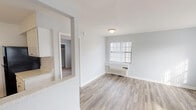 This single-floor space is designed with a clean, neutral aesthetic throughout, featuring soft grey walls and consistent light-toned finishes that create a cohesive and airy atmosphere. The living area is generously sized, showcasing smooth hardwood-style flooring that runs throughout the main living spaces. Natural light filters in through windows dressed with vertical blinds, and a wall-mounted HVAC unit ensures year-round comfort. The layout connects the living area to the kitchen via a pass-through opening, enhancing the sense of openness between spaces.

The kitchen is well-appointed with white cabinetry, speckled stone countertops, a double-basin stainless steel sink with a modern faucet, and a full-size black refrigerator. The space is practical and efficiently arranged for everyday use.

The bedroom features plush carpet flooring, a window with natural light, a built-in wall shelf, and a sliding closet. The room's neutral tones and simple design offer a calm retreat. The bathroom is finished in crisp white, with subway tile surround, a soaking tub, a vanity topped with stone counters, and modern brushed nickel fixtures, completing the space with a polished, functional design.