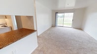 This single-floor unit offers a clean, functional layout designed to maximize comfort and usability. The spacious living area is finished with neutral-toned wall-to-wall carpeting and bright white walls, creating a light and airy atmosphere. A full-length sliding glass door floods the space with natural light while providing direct views of a lush green lawn and the surrounding community. The living area flows seamlessly toward the front entry, maintaining an open and uncluttered feel throughout.

The galley-style kitchen is efficiently arranged with white cabinetry lining both sides, offering generous storage and counter space. Granite-patterned laminate countertops complement the stainless steel sink and white refrigerator, while wood-look flooring adds warmth underfoot.

Two carpeted bedrooms each feature large windows that capture natural light and outdoor greenery, providing a tranquil setting. Both rooms offer ample wall space suited to a variety of furniture arrangements.

The unit includes two full bathrooms. The primary bath features a wide vanity with granite-patterned countertops, a large mirror with overhead lighting, wood-look flooring, and a tub-shower combination with white tile surround. A walk-through closet with wire shelving connects conveniently to the primary bath. The second bathroom mirrors a similarly clean, functional design.