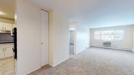 Located at 8528 Lotus Ave in Skokie, Illinois, this single-floor residence offers a well-organized layout with a clean, neutral aesthetic throughout. The living area is generously proportioned, featuring wall-to-wall carpeting in a warm beige tone, soft neutral walls, and a classic chandelier that anchors the dining area near the entryway. A closet provides convenient built-in storage, and a wall-mounted HVAC unit ensures year-round comfort. Natural light filters in through windows, offering views of the surrounding neighborhood. The kitchen has been thoughtfully updated with crisp white cabinetry, a grey mosaic tile backsplash, light marble-look luxury vinyl flooring, stainless steel appliances including a full-size refrigerator and gas range, and a decorative wine rack above the refrigerator. The bedroom is spacious and carpeted, with a large window that brings in ample daylight and a baseboard heating system along the perimeter. The bathroom is finished in a clean, all-white palette, featuring a single vanity with a mirrored medicine cabinet, a tub-shower combination with white tile surround, and classic white grid floor tile. The overall ambiance of the space is bright, practical, and move-in ready.