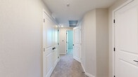 This single-story, 3-bedroom, 1-bathroom home offers a thoughtfully organized layout with clean, contemporary finishes throughout. The open kitchen is a standout feature, equipped with stainless steel appliances including a gas range, microwave, dishwasher, and refrigerator, complemented by crisp white cabinetry, light countertops, and warm light wood-style flooring. A central island provides additional prep and serving space, while multiple windows flood the area with natural light. The spacious living room features plush carpeting, a ceiling fan, and a glass-paneled door that opens to an outdoor area, bringing in additional natural light and views of the surroundings. The three bedrooms are carpeted and bright, each benefiting from natural light through well-positioned windows. The primary bedroom is generously sized and connects to a dedicated walk-in closet outfitted with wire shelving for ample storage. The bathroom is finished with light wood-style flooring, white cabinetry, and a glass-enclosed walk-in shower with white tile surround. A central hallway with recessed lighting and white paneled doors connects the private areas of the home, maintaining a cohesive and clean aesthetic. The overall palette of soft neutrals and white trim lends the home a bright, modern ambiance.