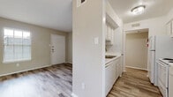 Located at 1541 Moritz Dr in Houston, Texas, this single-story unit offers a clean, neutral aesthetic carried throughout every room. Wood-look luxury vinyl plank flooring runs continuously across the living areas and bedrooms, providing a cohesive and low-maintenance foundation. The color palette is kept light and understated, with warm beige and off-white walls complemented by crisp white trim and baseboards.

The living area is generously proportioned, benefiting from a large window that draws in natural light and creates an open, airy atmosphere. The kitchen is efficiently laid out, featuring white cabinetry, a built-in sink, and a half-wall partition that separates it from the entry area, which includes a solid front door with secure hardware. The layout flows intuitively from the entry through the main living spaces and into the bedrooms.

The bedrooms are well-sized, each equipped with ceiling fans fitted with integrated lighting, and windows dressed with horizontal blinds. Closet access is provided in the bedrooms, adding practical storage. The bathroom is finished with white tile surrounding the shower-tub combination, a single-sink vanity with cabinetry below, a large wall mirror, and built-in shelving above the toilet. Overall, the unit presents a functional and move-in ready living environment.