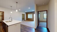 This single-floor residence offers a thoughtfully designed open-concept layout that seamlessly connects the kitchen, dining, and living areas. The kitchen is a standout feature, showcasing rich dark-stained cabinetry that reaches toward the ceiling, a full suite of stainless steel appliances including a refrigerator, range, and built-in microwave, and a generous island with a white countertop and integrated sink. Pendant lighting above the island adds a refined touch. Dark hardwood-style flooring runs throughout the kitchen and main living areas, creating a warm contrast against the light-toned walls.

The living area transitions to plush carpeting and features a large window with vertical blinds that invites natural light, along with recessed ceiling lights and an accent wall in a warm earthy tone. Two bedrooms continue the carpeted flooring and each include a ceiling fan with light fixture, vertical blind-covered windows with outdoor views of surrounding greenery, and ample wall space.

Both bathrooms are finished consistently with dark wood vanities, white countertops, single-basin sinks with brushed nickel fixtures, large mirrors, and shower-tub combinations. Rich wood-toned trim and six-panel doors appear throughout, tying the overall design together with a cohesive, contemporary aesthetic.