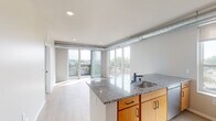 Located at 2225 E Lake St in Minneapolis, MN, this contemporary single-floor unit offers a thoughtfully designed open-concept layout filled with natural light. The living area is a standout feature, boasting expansive floor-to-ceiling windows and a sliding glass door that opens onto a private balcony, offering elevated views of the surrounding Minneapolis neighborhood. Exposed ductwork along the ceiling adds an industrial-modern character to the space.

The kitchen is well-appointed with granite countertops, warm-toned wood cabinetry, white upper cabinets, a blue tile backsplash, and a full suite of stainless steel appliances including a range, microwave, dishwasher, and refrigerator. A peninsula with a built-in sink connects the kitchen to the open living area, making it ideal for entertaining.

Light wood-style flooring runs throughout the main living areas and kitchen, while the bedroom features plush carpeting and a generously sized window with views of the tree-lined streetscape below. The bathrooms are finished with wood-toned vanity cabinetry, white countertops, matte black fixtures, and a tub-shower combination, all accented by wood-look flooring for a cohesive, clean aesthetic throughout the unit.
