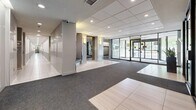 Located at 2 Silver Maple Crt in Brampton, Ontario, this building lobby serves as the welcoming gateway for residents and visitors alike. The space is thoughtfully designed with a clean, contemporary aesthetic, combining a neutral palette of grey and taupe tones with modern finishes throughout.

Upon entry, large floor-to-ceiling glass doors flood the vestibule with natural light, offering clear sightlines to the greenery outside. The flooring transitions between light-toned porcelain tile and durable commercial-grade carpet, clearly delineating traffic pathways. A drop ceiling with a recessed grid panel system and recessed pot lighting provides even, well-distributed illumination across the entire lobby.

A central seating alcove with a cushioned bench offers a comfortable waiting area for residents and guests, framed by structural columns with warm wall sconces. Framed artwork adds a touch of character to the space. To one side, a full bank of resident mailboxes lines the wall, providing convenient mail access directly from the lobby.

The elevator bank features multiple stainless steel elevator doors set against stylized tile accent walls, accompanied by digital display screens showing building information. The lobby also includes accessible amenities, as indicated by visible signage. A security camera system is discreetly integrated into the design, ensuring safety throughout the space.