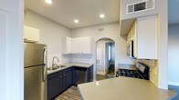 This single-floor space showcases a thoughtfully designed kitchen that balances modern aesthetics with practical functionality. The kitchen features a striking two-tone cabinet scheme, pairing crisp white upper cabinets with deep navy-toned lower cabinets, creating a bold yet cohesive visual contrast. A classic white subway tile backsplash runs along the walls, adding texture and a timeless design element to the space.

The countertops are finished in light quartz with subtle speckled detailing, providing durable and attractive work surfaces. A spacious kitchen island extends the prep area and adds versatility for dining or entertaining. Stainless steel appliances, including a refrigerator, gas range, built-in microwave, and dishwasher, lend a professional quality to the kitchen.

Recessed lighting illuminates the space efficiently from above, complementing the neutral grey walls and wood-look flooring that runs throughout. An elegant arched doorway leads to an adjoining room, adding an architectural detail that softens the otherwise modern interior. HVAC vents are integrated into the ceiling, ensuring a clean and uncluttered finish throughout the space.