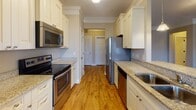 Located at 305 Advancement Ave in Durham, NC, this single-story unit offers a thoughtfully designed layout with a blend of hardwood and carpeted flooring throughout. The kitchen serves as a functional centerpiece, featuring stainless steel appliances including a French door refrigerator, dishwasher, electric range, and built-in microwave. Cream-toned cabinetry extends to the ceiling, providing generous storage, while granite countertops with an extended breakfast bar add both utility and style. Pendant lighting over the sink area enhances the kitchen's warm ambiance, and a window offers natural light and exterior views.

The open living and dining area is defined by elegant crown molding, soft neutral tones, and plush carpeting. Large windows allow abundant natural light while offering neighborhood views. The bedrooms continue the carpeted aesthetic, each equipped with ceiling fans and ample windows. A built-in desk and cabinetry nook adds a versatile workspace within the unit.

The bathrooms are well-finished, with the primary bath featuring a dual-sink granite vanity with cream cabinetry, large mirrors, and tile flooring. A secondary bath includes a tub-shower combination with brushed nickel fixtures. The overall design is cohesive, clean, and functional throughout.