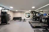 Located at 1644 Malcolm Ave in the Westwood neighborhood of Los Angeles, this contemporary fitness center is thoughtfully designed to support a wide range of workout routines. The space is finished with smooth, neutral-toned walls and durable flooring throughout, creating a clean and professional atmosphere. Recessed round lighting fixtures are evenly distributed across the ceiling, providing bright, consistent illumination across the entire floor.

The cardio zone features multiple treadmills equipped with individual digital screens, alongside a stationary cycling bike, offering users a variety of aerobic options. A dedicated TRX Training Zone is prominently positioned and fully stocked with kettlebells, medicine balls, and suspension training straps, catering to functional and strength-based workouts. A dumbbell rack with a broad range of weights, a flat bench, and a BOSU balance trainer support free weight and core training needs.

Floor-to-ceiling mirrors are strategically placed to enhance the sense of space and allow users to monitor their form during exercise. A wall-mounted folding mat provides additional flexibility for floor-based training. A water station and restroom are conveniently accessible within the facility. Natural light filters in through a horizontal window, adding a refreshing connection to the outdoors. The overall design is modern, functional, and well-equipped for comprehensive fitness training.