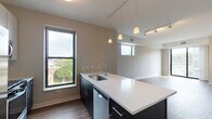 This 2-bedroom, 2-bathroom "L"-shaped residence is thoughtfully designed with a contemporary open-concept layout that seamlessly connects the kitchen and living areas. The kitchen serves as the centerpiece of the main living space, featuring a large island with a white quartz countertop, dark cabinetry, stainless steel appliances including a French door refrigerator, gas range, built-in microwave, and dishwasher. White upper cabinets provide ample storage, while pendant lighting adds a stylish accent above the island. Rich hardwood flooring extends throughout the main living and dining areas, complemented by track lighting overhead. The spacious living room is filled with natural light from multiple windows and a sliding glass door that opens to a private balcony with outdoor views. Both bedrooms are carpeted and generously sized, each featuring large windows that bring in abundant natural light and views of the surrounding area. The bathrooms are finished with dark wood vanities, white quartz countertops, undermount sinks, and walk-in tile showers. Additional features include a walk-in closet and a neutral warm-toned color palette throughout, creating a clean and modern aesthetic.