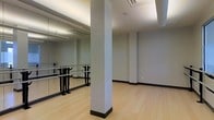 Located at 4115 Britton Parkway in Hilliard, Ohio, this single-floor studio space is thoughtfully designed for fitness, dance, or movement-based activities. The interior showcases a clean, contemporary aesthetic with neutral gray walls that create a calm and focused atmosphere throughout.

The primary feature of the space is a spacious open exercise room finished with smooth, light-toned hardwood flooring that provides both durability and an inviting warmth underfoot. A full-length wall mirror runs the length of one side of the room, paired with professional ballet barres — ideal for dance instruction, barre fitness classes, or stretching routines. The mirror visually expands the room while allowing participants to monitor their form and technique.

Structural support columns are integrated into the layout and finished in the same neutral palette, maintaining a cohesive and uncluttered look. The ceiling features a recessed tray design with built-in lighting that provides even, diffused illumination across the space, complemented by ceiling-mounted speakers and ventilation units that enhance comfort during active use.

Overall, the space offers a professional, well-appointed environment suited for fitness instruction, dance classes, or personal training, combining functional design with a polished, modern finish.