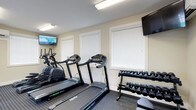 Located at 1655 Gilmore Park Ave in Columbus, Ohio, this fitness center offers a clean, well-organized workout environment designed to support a variety of exercise routines. The single-floor facility is thoughtfully laid out to maximize usability and comfort for its users.

The workout area is equipped with multiple treadmills and an elliptical machine, providing ample options for cardiovascular training. A dedicated free weights section features a fully stocked dumbbell rack with a wide range of weight options, catering to both beginner and experienced fitness enthusiasts. Rubber flooring throughout the workout space provides safety and stability during exercise.

Two wall-mounted flat-screen televisions are positioned for easy viewing from the cardio equipment, allowing users to stay entertained during workouts. The space is well-lit with overhead fluorescent lighting, ensuring a bright and functional environment at any time of day.

Natural light is introduced through multiple windows fitted with white horizontal blinds, contributing to the open and airy feel of the room. The neutral color palette of the walls and clean aesthetic of the space create a focused, distraction-free atmosphere conducive to an effective workout. Overall, this fitness center provides a practical and inviting setting for daily exercise.