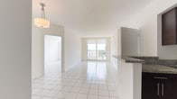 Unit 602 is a single-floor residence designed with a clean, contemporary aesthetic and a bright, airy atmosphere throughout. White large-format ceramic tile flooring runs consistently across all living areas, reflecting natural light and reinforcing the open, cohesive feel of the space.

The living and dining area is expansive and open, anchored by a sliding glass door that leads to a balcony and frames sweeping outdoor views of the surrounding cityscape. A pendant light fixture adds a refined touch to the dining area. The kitchen is designed in a galley configuration, featuring rich dark espresso cabinetry, granite countertops, and a full suite of stainless steel appliances including a refrigerator, range, microwave, and dishwasher. A pass-through counter connects the kitchen to the main living area.

The bedrooms are generously proportioned and sun-filled, each with large windows offering city and sky views, roller shades, and tile flooring. The primary bathroom includes a glass-enclosed walk-in shower with mosaic tile detailing, while the secondary bathroom features a full soaking tub with a tiled surround, a granite-topped vanity with integrated sink, and a large mirror. An in-unit laundry area is also present, adding practical convenience to this well-appointed residence.