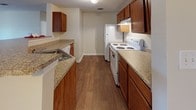 This upgraded single-story residence offers three bedrooms and two full bathrooms within a well-organized, functional floor plan. The living area features warm wood-look hard-surface flooring and connects openly to the kitchen, creating a cohesive common space suitable for both everyday living and entertaining.

The kitchen is equipped with rich wood cabinetry, granite-style countertops, a double-basin sink, and white appliances including a range and refrigerator. A breakfast bar provides a convenient pass-through to the living area, enhancing the open feel of the space.

Each of the three bedrooms features plush neutral carpeting and windows fitted with blinds that allow natural light while maintaining privacy. Select bedrooms include closets with built-in rods for organized storage. The rooms offer comfortable proportions with clean, neutral wall tones throughout.

Both bathrooms are finished with wood-look flooring, oak-toned vanity cabinetry, granite-style countertops, and tub-shower combinations. Wall-mounted mirrors and vanity lighting complete each bathroom's practical design.

Overall, the home presents a consistent, neutral aesthetic with upgraded finishes that provide a move-in ready environment.