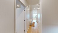 Located at 200 W Ocean Blvd in Long Beach, California, this single-floor residence showcases a clean, contemporary design defined by white walls, light hardwood flooring, and recessed lighting throughout. The open-concept kitchen is a standout feature, equipped with stainless steel appliances including a gas range, microwave, and dishwasher, complemented by warm natural wood cabinetry, white quartz countertops, and a breakfast bar with modern bar seating. Open shelving adds a functional yet decorative touch, while tall ceilings amplify the sense of volume in the space. A light-filled hallway with frosted glass doors connects the living areas to the private quarters, maintaining a seamless flow through the unit. The bedroom is a well-appointed retreat, featuring ample wall space accentuated by vibrant, curated artwork and warm bedside lighting. The bathroom is finished with large-format tile flooring, a floating wood vanity with an illuminated mirror, a walk-in shower, and a sculptural soaking tub — a refined combination of form and function. Floor-to-ceiling windows visible from the bedroom corridor invite abundant natural light and offer outward views, enhancing the airy, modern ambiance that defines this thoughtfully designed Long Beach residence.