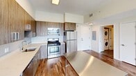 Located in Stamford, CT, this modern two-bedroom, one-bathroom residence offers a well-designed layout across a single floor. Rich hardwood flooring runs throughout the living spaces, complementing the clean, contemporary aesthetic defined by crisp white walls and neutral tones.

The combined kitchen and living area serves as the heart of the home. The kitchen is outfitted with wood-grain cabinetry, sleek light quartz countertops, and a full suite of stainless steel appliances including a gas range, built-in microwave, dishwasher, and refrigerator. A stainless steel island provides additional prep and dining space. Conveniently tucked nearby is a stacked in-unit washer and dryer.

Both bedrooms are generously proportioned, with the primary bedroom offering notably expansive floor space. Each room features large, floor-to-ceiling gridded windows that flood the interiors with natural light and frame elevated views of Stamford's cityscape and surrounding greenery.

The bathroom is finished with modern white cabinetry, a wide vanity with a white countertop, a large mirror with contemporary lighting fixtures, and grey tile flooring. A closet provides additional storage within the unit.

This residence combines functional design with modern finishes, making it a comfortable and stylish home in the heart of Stamford.