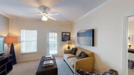 This thoughtfully designed 2-bedroom, 2-bathroom residence offers a comfortable and functional single-floor layout. The living room features plush carpeting, crown molding, a ceiling fan, and a glass door that opens to an outdoor area, allowing natural light to fill the space. Adjacent to the living room, a dedicated dining area stands out with its blue accent wall, chair rail molding, and elegant pendant light fixture overhead.

The kitchen is well-appointed with rich wood cabinetry, dark granite-style countertops, black appliances including a refrigerator, range, and dishwasher, and a breakfast bar that connects to the main living areas. Light tile flooring completes the kitchen's polished look.

The primary bedroom is generously sized with soft carpet, a ceiling fan, and large windows dressed with decorative curtains, creating a warm and restful retreat. The second bedroom features its own distinctive style, highlighted by an ornate wrought-iron headboard and ample natural light. Each of the two full bathrooms includes a tub-shower combination, a vanity with granite-style countertops, warm wood cabinetry, and tile flooring, providing practical comfort throughout.