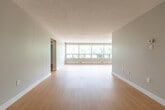 Located at 750 Wonderland Rd S in London, Ontario, this one-bedroom, one-bathroom unit offers a thoughtfully laid-out single-floor living space. The interior is finished with light hardwood flooring throughout, neutral grey and white walls, and textured ceilings, creating a clean and consistent aesthetic.

The living room is a standout feature, boasting a wide, multi-panel window that spans much of the exterior wall, filling the space with abundant natural light and offering pleasant views of the surrounding mature trees. This open area flows naturally toward the kitchen, where a stainless steel refrigerator, white upper and lower cabinetry, a grey countertop, and a double sink come together in a functional galley-style layout.

The bedroom is a comfortable, well-proportioned room with soft neutral tones and large sliding panel closet doors that maximize storage while maintaining a streamlined look. The bathroom is finished with white wall tiles surrounding a full bathtub with a showerhead and chrome fixtures, maintaining the space's clean and minimalist character.

A connecting hallway ties the rooms together efficiently, contributing to the unit's practical flow. Overall, this space presents a bright, low-maintenance living environment well-suited to those seeking simplicity and comfort in a residential London neighbourhood.