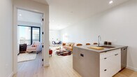 This single-floor residence is designed with a contemporary aesthetic, combining clean lines, neutral tones, and thoughtfully selected materials throughout. The open-concept layout connects the kitchen, dining, and living areas, creating a cohesive and functional living space filled with natural light.

The kitchen is well-appointed with stainless steel appliances, including a range, microwave, and refrigerator. Light wood upper cabinetry contrasts with crisp white lower cabinets, and a marble-style backsplash adds visual interest. A substantial concrete-finish island with bar seating serves as both a workspace and gathering point, seamlessly bridging the kitchen and living area.

The living and dining zone is bright and open, featuring recessed lighting, white walls, and light hardwood flooring that runs throughout the unit. Large windows allow natural light to flow into the space, contributing to an airy, welcoming ambiance.

The bedroom is calm and well-proportioned, with a window offering outdoor views and ample space for furnishings. Two bathrooms are finished with stone-tile flooring and warm wood vanities on black metal frames. One bathroom includes a glass-enclosed shower, while the other features a soaking tub, both maintaining a consistent, modern design language.