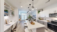 Located at 12455 Research Blvd in Austin, TX, this thoughtfully designed one-bedroom, two-bathroom residence offers a modern aesthetic with clean lines and a bright, cohesive palette throughout. The open-concept living and kitchen area serves as the heart of the home, where light wood-tone flooring, recessed lighting, and white walls create an airy, welcoming atmosphere. The kitchen is a standout feature, showcasing two-tone cabinetry in white and gray, subway tile backsplash, stainless steel appliances, and a generous center island with a built-in sink, seating, and striking pendant lights overhead. The space flows seamlessly into the living room, which is anchored by French doors topped with transom windows that invite natural light and lead to the outdoors. The bedroom is a serene retreat with a ceiling fan, a window with outdoor views, and ample space for rest and relaxation. One bathroom features a tub-shower combination with clean white tile and a built-in niche, while the primary bathroom offers a long vanity with dual sinks, matte black fixtures, and convenient in-unit laundry. A dedicated closet adds practical storage. Together, these spaces deliver a well-appointed, efficient, and stylish home in the heart of Austin.