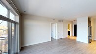 This single-floor space showcases a contemporary design with a clean, minimalist aesthetic throughout. The open main living area is finished with light-toned hardwood-style flooring that extends across the space, contributing to a bright and airy atmosphere. Smooth white ceilings with recessed lighting provide even illumination, while neutral warm-beige walls create a calm and versatile backdrop.

Visible HVAC vents are thoughtfully integrated into both the ceiling and walls, ensuring comfort throughout the space. White interior doors with simple, modern hardware provide access to additional rooms, including what appears to be a closet and a hallway leading to further private areas. A glimpse down the hallway reveals a bathroom with dark cabinetry and warm accent lighting, offering a striking contrast to the lighter tones found in the main living area.

The layout is practical and well-organized, with clearly defined zones that allow for flexible use of the space. The transitions between rooms are clean and unobstructed, supporting an easy flow throughout. Overall, the space presents a move-in-ready environment with modern finishes and a functional single-level floor plan well-suited to a variety of living arrangements.