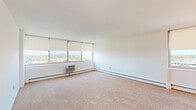 Located at 2400 McClellan Ave in Pennsauken, NJ, this single-floor unit offers a well-organized layout with multiple living spaces, a functional kitchen, a full bathroom, and generously sized rooms throughout. The galley-style kitchen is equipped with warm wood cabinetry, light stone-finish countertops, a gas range, dishwasher, refrigerator, and a stainless steel sink — all set atop tile flooring with a skylight-style overhead fixture providing bright, even illumination. A window at the end of the kitchen frames outdoor views and allows natural light to flow through the space. The living areas feature neutral wall-to-wall carpeting and clean white walls, creating a bright and open atmosphere. Large windows fitted with roller shades are a standout feature throughout, offering expansive views of the surrounding landscape and distant city skyline — a hallmark of the elevated position of this unit. Each room benefits from individual wall-mounted HVAC units and baseboard heating for year-round climate control. The bedroom includes a full closet with bifold doors, providing ample storage. The bathroom is appointed with a vanity featuring a dark countertop, mirrored medicine cabinet, mosaic tile flooring, and a full soaking tub with an overhead shower.
