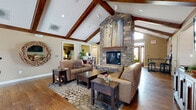 Located at 12929 Delaware Pkwy in Kansas City, KS, this single-floor community clubhouse offers a warm and inviting atmosphere anchored by a striking floor-to-ceiling stacked stone fireplace. The soaring vaulted ceiling with rich exposed wooden beams defines the main living area, where hardwood flooring and comfortable leather seating create an welcoming gathering space. Large artwork adorns the fireplace surround, adding a contemporary artistic touch to the rustic design.

The lounge area extends into a carpeted sitting room filled with natural light from multiple windows, furnished with plush sectional seating, a wall-mounted flat-screen television, and colorful accent chairs with ottomans. A dedicated game room features a full-sized billiard table, wall-mounted cue rack, and an additional flat-screen television for entertainment.

A private meeting or business room provides a large conference-style table, desk area, and ample natural light, suited for gatherings or work sessions. The fully equipped kitchen includes dark wood cabinetry, granite countertops, stainless steel appliances, and a coffee station. Near the main entrance, high-top bar seating flanks elegant double doors with decorative glass sidelights, completing this well-appointed and functional community space.