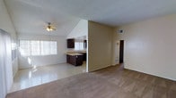 This single-floor home offers 2 bedrooms and 1.5 bathrooms within an open and airy layout designed for comfortable everyday living. The main living area is anchored by striking vaulted ceilings that lend a spacious, expansive feel to the room. A ceiling fan with light fixture is mounted at the peak, adding both function and a casual aesthetic. The living space features neutral-toned carpet that flows throughout much of the home, while tile flooring defines the kitchen and dining areas for easy maintenance. Natural light filters in through large windows dressed with vertical blinds, brightening the open floor plan. The kitchen is seamlessly integrated into the living space and features dark espresso-toned cabinetry, a peninsula with sink, and light-colored countertops — creating a practical and visually grounding contrast against the warm beige walls. A textured ceiling adds subtle architectural character throughout. The hallway leads to the bedrooms and bathrooms, offering a clear and logical flow through the home. With its open-concept design, vaulted ceilings, and functional kitchen layout, this home provides a welcoming and well-organized living environment.