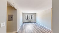 This 2-bedroom, 1-bathroom apartment offers a well-organized layout across a single floor, making efficient use of its compact footprint. The living area features light wood-style laminate flooring and neutral grey-toned walls, creating a clean, contemporary aesthetic. A window with black-framed trim allows natural light to filter in while offering views of the surrounding urban cityscape, including neighboring mid-rise buildings and rooftops. A wall-mounted HVAC unit provides in-unit climate control.

The kitchen is thoughtfully appointed with grey shaker-style cabinetry, white quartz countertops, a classic subway tile backsplash, and a full suite of stainless steel appliances including a range, microwave, and dishwasher.

The primary bedroom is generously sized and includes a sliding-door closet, while the secondary bedroom offers its own closet and connects to the hallway. Both rooms continue the light flooring found throughout the unit.

The bathroom is finished with white square tile surrounding a tub-shower combination, a compact vanity with dark hardware, and a mirror with modern overhead lighting. Clean white walls and consistent flooring tie the space together throughout.