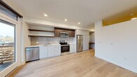 Located on North Broadway Street in Tacoma, WA, this thoughtfully designed one-bedroom, one-bathroom residence offers a contemporary living experience within a compact, efficiently arranged floor plan. Light hardwood flooring flows consistently throughout, lending warmth and visual continuity to every room.

The open-concept kitchen and living area serves as the heart of the home. The kitchen is outfitted with a full suite of stainless steel appliances—including a dishwasher, electric range, microwave, and refrigerator—complemented by sleek white lower cabinetry, dark wood upper cabinets, floating open shelves, a tile backsplash, and crisp white countertops. A large window fills the kitchen with natural light and provides outdoor views.

The living area is bright and open, featuring recessed lighting and a distinctive architectural detail with a warm yellow ceiling accent, adding a subtle pop of character. A built-in desk nook provides a functional workspace.

The bedroom is a calm, well-proportioned retreat with a floor-to-ceiling window and sliding glass door opening to a private balcony with views of the surrounding Tacoma neighborhood. A sliding-door closet with built-in shelving provides ample storage.

The bathroom features a wide vanity with a white countertop, undermount sink, large mirror, and light hardwood-style flooring, maintaining the clean, modern aesthetic found throughout the space.