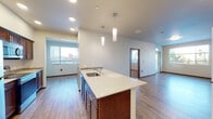 This well-designed single-floor residence offers a thoughtful layout that balances open living areas with private spaces. At the heart of the home is an open-concept kitchen and living area, where rich dark cabinetry is paired with light quartz countertops and a full suite of stainless steel appliances, including a refrigerator, range, and over-the-range microwave. A generous kitchen island with an undermount sink serves as a functional centerpiece, illuminated by sleek pendant lighting that adds a modern touch. Hardwood-style flooring flows throughout the main living areas, complemented by recessed lighting and large windows that invite abundant natural light and outdoor views. The living space extends seamlessly toward multiple access points, creating an airy, connected feel. The bedrooms offer comfortable carpeted flooring and sizable windows with outdoor views, providing a calm and restful atmosphere. Two bathrooms echo the home's design language, featuring rich wood vanity cabinetry, quartz countertops, undermount sinks, large mirrors, and tile accent backsplashes. The overall aesthetic throughout is clean and contemporary, with neutral tones, warm wood accents, and consistent finishes that create a cohesive and inviting living environment.