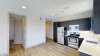 Located at 1516 Xavier Street in Denver's vibrant 80204 corridor, this single-floor residence offers a clean, contemporary design with an open-concept living and kitchen layout. The kitchen is well-appointed with stainless steel appliances — including a gas range, microwave, refrigerator, and dishwasher — complemented by sleek dark cabinetry that contrasts sharply against light-toned countertops and a classic subway tile backsplash. Track lighting overhead provides focused illumination throughout the cooking and living areas. Smooth light wood-style flooring runs continuously across the space, lending warmth and visual continuity. The living area is generously proportioned, benefiting from abundant natural light streaming through multiple windows fitted with horizontal blinds. A sliding glass door connects the interior to an outdoor space, further enhancing the sense of openness and providing easy access to fresh air and exterior views. Neutral wall tones and recessed lighting contribute to the bright, airy ambiance throughout. The overall design aesthetic is modern and functional, making efficient use of the open floor plan while maintaining a comfortable and inviting atmosphere.