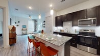 Located at 6001 S Congress Ave in Austin, Texas, this single-floor residence offers a well-designed open-concept layout that seamlessly connects the kitchen, dining, and living areas. The kitchen is a standout feature, equipped with rich dark cabinetry, granite countertops, a mosaic tile backsplash, stainless steel appliances, and a large central island with pendant lighting — ideal for both cooking and casual dining. Light wood-style flooring runs throughout the main living areas, adding warmth and continuity to the space. The living room is bright and inviting, with large windows that allow generous natural light, built-in wall shelving, a ceiling fan, and a comfortable modular sofa. The bedroom is a creative retreat, featuring plush carpeting, large windows, and ample wall space. The bathroom offers a full tub-shower combination with tile surround, a granite-topped vanity with dark cabinetry, and access to a dedicated walk-in closet with built-in shelving. Throughout the residence, the design balances modern finishes with a functional, livable layout, making it a compelling option in the South Austin area.