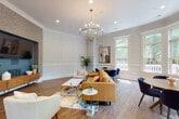 This single-floor amenity space masterfully combines traditional architectural elements with modern interior design across several interconnected areas. The entrance lounge sets a striking tone with soaring ceilings, rich dark-wood wainscoting, and floor-to-ceiling windows framed in mahogany trim, flooding the space with natural light and offering views of mature surrounding trees. Textured botanical wallpaper, pendant lighting, and mid-century-inspired seating in warm terracotta velvet create an inviting, upscale atmosphere.

Transitioning inward, a spacious lounge area features crisp white wainscoting panels, elegant crown molding, and hardwood flooring throughout. A brass chandelier anchors the room above a curated seating arrangement of caramel leather and neutral upholstered furniture, centered around a marble-topped coffee table. A built-in media wall with textured tile surround adds a contemporary focal point.

The game room offers a more casual atmosphere, centered around a full-size billiards table beneath a cluster of modern globe pendant lights. French doors connect this area to an outdoor patio, ensuring excellent flow and ventilation. A cozy nook with a navy leather sofa and textured accent wall provides a relaxed retreat within the space.