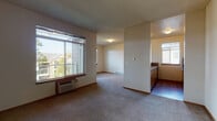 Located at 5015 South Regal Street in Spokane, WA, this single-floor unit offers a practical and well-organized open-concept layout. The living area is generously sized, finished with neutral-toned carpet throughout, and receives abundant natural light through large sliding windows that frame views of the surrounding neighborhood and mature trees. A wall-mounted HVAC unit provides climate control directly in the living space.

The kitchen is defined by a peninsula-style breakfast bar that separates it from the living and dining areas, creating a semi-open feel while maintaining distinct zones. It is equipped with black appliances, including a refrigerator, electric range, and over-the-range microwave, complemented by warm wood cabinetry and tile backsplash. The kitchen also features hardwood flooring, contrasting with the carpeted areas of the unit.

A hallway with warm wood trim connects the main living areas to the private spaces, including a bathroom finished with tile flooring, a full tub/shower combination, and a vanity with mirror. The textured ceilings, neutral wall tones, and consistent warm wood accents throughout give the unit a cohesive and understated aesthetic. The overall layout is efficient, making thoughtful use of the available space across its single floor.