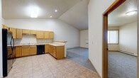 Located at 5050 40th Ave S in Fargo, North Dakota, this 1-bedroom, 1-bathroom unit offers a functional and comfortable layout across a single floor. The kitchen is a standout feature, boasting vaulted ceilings that lend an open, airy feel to the space. Warm honey-toned oak cabinetry lines the walls, providing ample storage, while a peninsula counter offers additional workspace and a natural transition into the living area. Black appliances — including a refrigerator, range, microwave, and dishwasher — complement the cabinetry, and tile flooring runs throughout. The living area transitions seamlessly from the kitchen and features plush carpeting. The generously sized bedroom includes carpet flooring, a window for natural light, and a baseboard heater. The full bathroom is well-proportioned, featuring a tub-shower combo, toilet, and a wood-toned vanity with a single sink. Directly accessible from the bathroom is a spacious walk-in closet outfitted with wire shelving for organized storage. A dedicated laundry room houses a full-size washer and dryer, adding significant everyday convenience. Warm wood trim throughout ties the space together with a cohesive, traditional aesthetic.