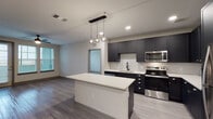Located at 14680 Westerly Dr in Winter Garden, FL, this single-floor 2-bedroom, 2-bathroom residence offers a well-designed layout with modern finishes throughout. The open-concept kitchen serves as the centerpiece of the living area, showcasing dark charcoal shaker-style cabinetry, bright white quartz countertops, and a herringbone-patterned tile backsplash. A central island with pendant globe lighting provides additional prep space and a natural gathering point. Stainless steel appliances, including a refrigerator, range, microwave, and dishwasher, complete the kitchen. Light wood-look plank flooring runs through the main living areas, adding warmth and continuity. Both bedrooms feature plush carpet flooring, natural light from double windows with blinds, and ceiling fans. The primary bathroom offers a sleek glass-enclosed walk-in shower with large-format white tile and matte black fixtures. The second bathroom includes a full tub-shower combination, dark vanity cabinetry, white countertops, and light wood-look flooring. The overall aesthetic is clean and contemporary, with a neutral color palette that creates a bright, cohesive atmosphere throughout the home.