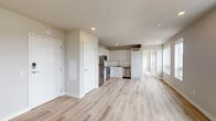 This thoughtfully designed single-floor unit offers a clean, modern aesthetic throughout, anchored by light-toned luxury vinyl plank flooring that runs seamlessly across all living areas. The open-concept layout connects the entry and living space directly to the kitchen, which is outfitted with white shaker-style cabinetry, dark countertops, and a full suite of stainless steel appliances including a refrigerator, electric range, microwave, and dishwasher. Recessed lighting illuminates the kitchen and common areas, enhancing the bright, airy atmosphere. The living area is generously proportioned and benefits from a row of large windows that invite abundant natural light and offer views of the surrounding neighborhood. The bedrooms continue the neutral palette, featuring soft walls, recessed lighting, and built-in storage cabinetry, with windows providing additional natural light and ventilation. The bathrooms are finished with white subway tile walk-in showers equipped with ceiling-mount and handheld fixtures, brushed nickel hardware, and clean, minimalist vanities. Accessibility features, including grab bars in the shower areas, are thoughtfully incorporated. The overall ambiance is contemporary and move-in ready, with a cohesive design language of whites, soft greys, and warm wood tones throughout.