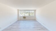 This thoughtfully renovated single-floor residence offers a clean, modern aesthetic throughout, defined by crisp white walls, light hardwood flooring, and an abundance of natural light. The open living area is a standout feature, anchored by large picture windows that frame sweeping views of the surrounding hillside and neighborhood below, creating a bright and airy atmosphere. A wall-unit air conditioner ensures year-round comfort in the main living space.

The kitchen is sleek and highly functional, featuring high-gloss white cabinetry extending to the ceiling, light quartz countertops, recessed lighting, and a full suite of stainless steel appliances including a refrigerator, electric range, built-in microwave, and dishwasher. The layout provides ample counter space and storage, making it well-suited for everyday cooking.

The bedrooms are generously proportioned, with the same light hardwood flooring and neutral white walls that carry throughout the unit. Multiple windows in the bedroom areas continue the theme of natural light and hillside views, with one room featuring a mirrored closet. The bathroom is neatly appointed with a white vanity, tile flooring, recessed lighting, a large mirror, and a glass-enclosed shower and tub combination. Overall, the space presents a cohesive, contemporary feel with clean finishes throughout.