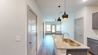 This thoughtfully designed single-story residence offers a cohesive one-bedroom, one-bathroom floor plan with modern finishes throughout. The open-concept kitchen serves as a focal point, featuring dark espresso cabinetry, granite countertops, a subway tile backsplash, stainless steel appliances including a side-by-side refrigerator with ice dispenser, and a central island with an undermount sink topped by stylish pendant lighting. Wood-look flooring flows seamlessly through the kitchen and living areas, creating a warm, unified aesthetic. The living room is bright and airy, benefiting from a ceiling fan and direct access to an outdoor balcony through a glass door flanked by windows that invite abundant natural light. The generously sized bedroom is finished with plush carpet, a ceiling fan, and a window with outdoor views. It connects conveniently to a dedicated closet and a well-appointed bathroom featuring a dual-sink granite vanity with dark cabinetry and a large mirror. The closet offers additional dedicated storage. Clean white walls, panel-style doors, and consistent hardware choices throughout contribute to a cohesive and contemporary overall ambiance.