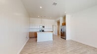 Located at 5602 Shadow Hills Rd in Las Cruces, NM, this single-story, 2-bedroom, 3-bathroom home offers a clean, modern design with a bright and airy feel throughout. The open-concept layout seamlessly connects the living room, dining area, and kitchen into one cohesive gathering space, highlighted by soaring ceilings and recessed lighting. The kitchen is a standout feature, boasting a large central island with a white quartz countertop and sink, a mix of white upper cabinets and warm wood-toned lower cabinetry, and a full suite of stainless steel appliances including a French door refrigerator, range, and built-in microwave. Light wood-look flooring flows consistently through every room, adding warmth and continuity. The primary bedroom is generously sized with its own dedicated closet and an en suite bathroom featuring an accessible roll-in shower with grab bars. The second bedroom is bright and well-proportioned, benefiting from natural light through large windows. A second full bathroom includes a soaking tub and shower combination. A dedicated laundry area and additional closets provide practical storage. The home's clean white walls and neutral palette create a fresh, move-in-ready atmosphere throughout.