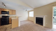 This single-floor residential unit offers a well-organized and functional layout designed for comfortable everyday living. The open-concept living area serves as the heart of the home, featuring warm neutral tones, plush wall-to-wall carpeting, and a classic wood-mantel fireplace that anchors the room. A ceiling fan provides year-round comfort, while a large window and sliding glass door flood the space with natural light and provide access to a private balcony with outdoor views. The seamless transition between the living area and kitchen makes the space feel open and connected. The kitchen is thoughtfully equipped with light maple cabinetry offering generous storage, laminate countertops, wood-look flooring, and black appliances including a range, over-the-range microwave, refrigerator, and dishwasher. A breakfast bar peninsula bridges the kitchen and living space, ideal for casual dining. Track lighting overhead ensures the workspace is well-lit. The bedroom is a calm, carpeted retreat with a broad window that welcomes natural light and a baseboard heater for added warmth. The bathroom is clean and straightforward, featuring a full soaking tub with a shower, toilet, and neutral finishes throughout. Textured ceilings are consistent across the unit, adding subtle depth to each room.