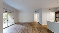 This single-floor residence offers a clean, contemporary design highlighted by warm wood-look flooring that extends throughout the living areas, bedroom, and kitchen. The open living and dining area is generously sized, featuring neutral white walls, crown molding, and multiple windows dressed with blinds that invite abundant natural light. A full-width sliding glass door leads to a private balcony enclosed by a decorative iron railing, providing pleasant views of surrounding greenery.

The galley-style kitchen is well-equipped with rich dark wood cabinetry, white quartz countertops, a subway tile backsplash, and a full suite of stainless steel appliances including a refrigerator, range, microwave, and dishwasher. A peninsula with an undermount sink and pendant lighting adds both functionality and style.

The bedroom is a bright, comfortable space with a ceiling fan, a window overlooking greenery, and continued wood-look flooring. The bathroom features a full tub and shower combination with white tile surround, a white quartz vanity top with dark wood cabinetry, and wood-look flooring. A dedicated entryway and interior hallway connect the spaces efficiently, completing the practical and cohesive layout.