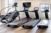 This 1,360 square foot fitness center, located at 1554 Midway Pkwy in Saint Paul, MN, offers a state-of-the-art exercise experience. The single-floor facility boasts an open, industrial-inspired design with exposed ceiling infrastructure and ample lighting. The space is thoughtfully divided into distinct workout zones, each equipped with specialized machinery. Cardio enthusiasts will find multiple treadmills, ellipticals, and rowing machines, while strength training areas feature weight racks, benches, and resistance equipment. The center incorporates modern technology with integrated screens on various machines. Large windows allow natural light to flood the space, creating an energizing atmosphere. The flooring alternates between cushioned surfaces for comfort and durability. Additional amenities include strategically placed fans for air circulation and a separate area visible through an interior window, possibly for staff or specialized training. This well-equipped gym provides a comprehensive fitness solution in a clean, contemporary setting.